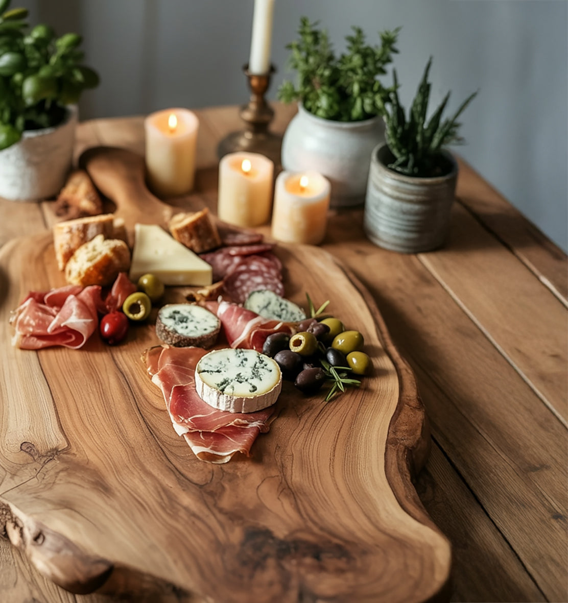 Charcuterie board with assorted cheeses, cured meats, olives, and bread on wooden table with candles and potted herbs