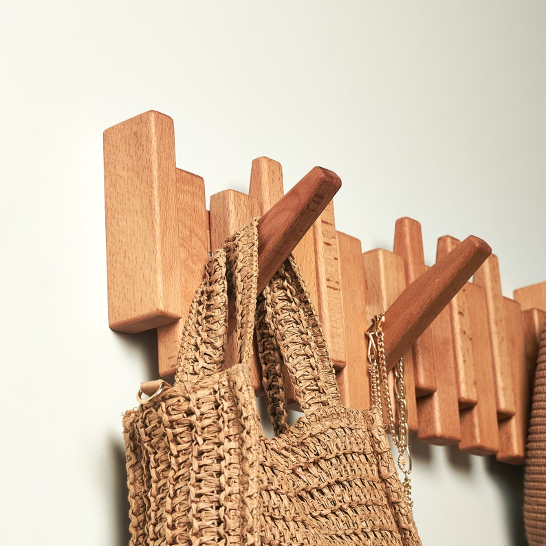 wooden wall-mounted coat rack with wooden pegs holding woven bag and gold chain accessories