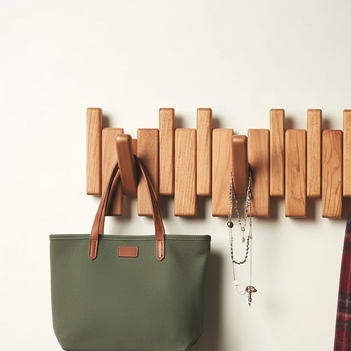 Wooden wall coat rack with asymmetrical hooks holding green tote bag and hanging necklaces