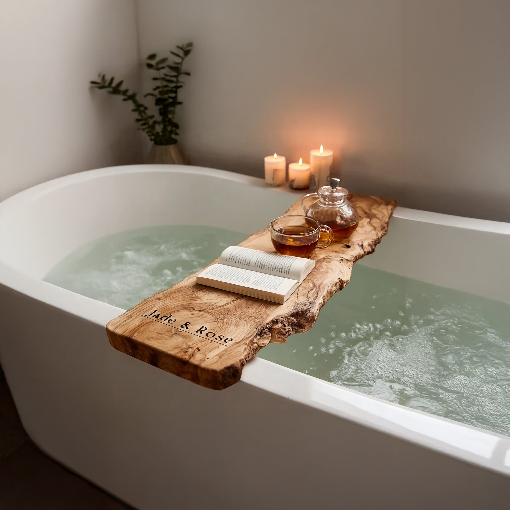 Rustic wooden bathtub tray over white filled bathtub with book, teapot, cup, and lit candles
